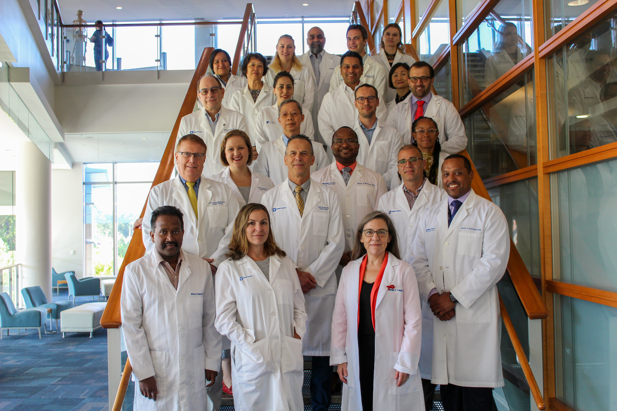 Division of Surgical Sciences faculty stand for a group photo in their white coats on the stairs of Trent Semans Center