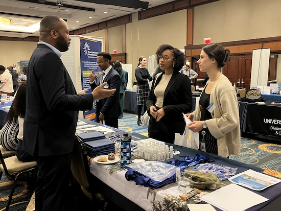 A man speaks with two women at an event exhibition table