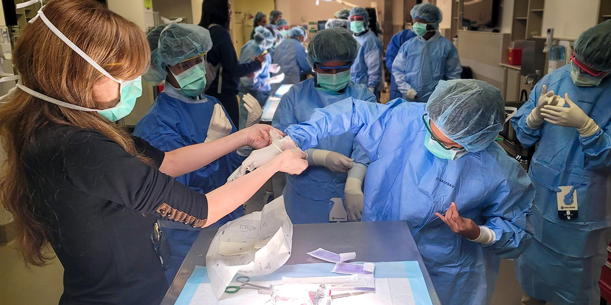 Photo of Dr. Cendales helping a young student put on gloves as other fully gowned students look on