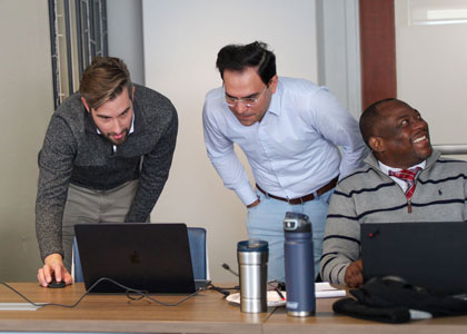 Photo of two HSR team members collaborating around a laptop and a third speaking with another off-frame