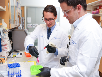 Two men in white lab coats conduct research in a lab