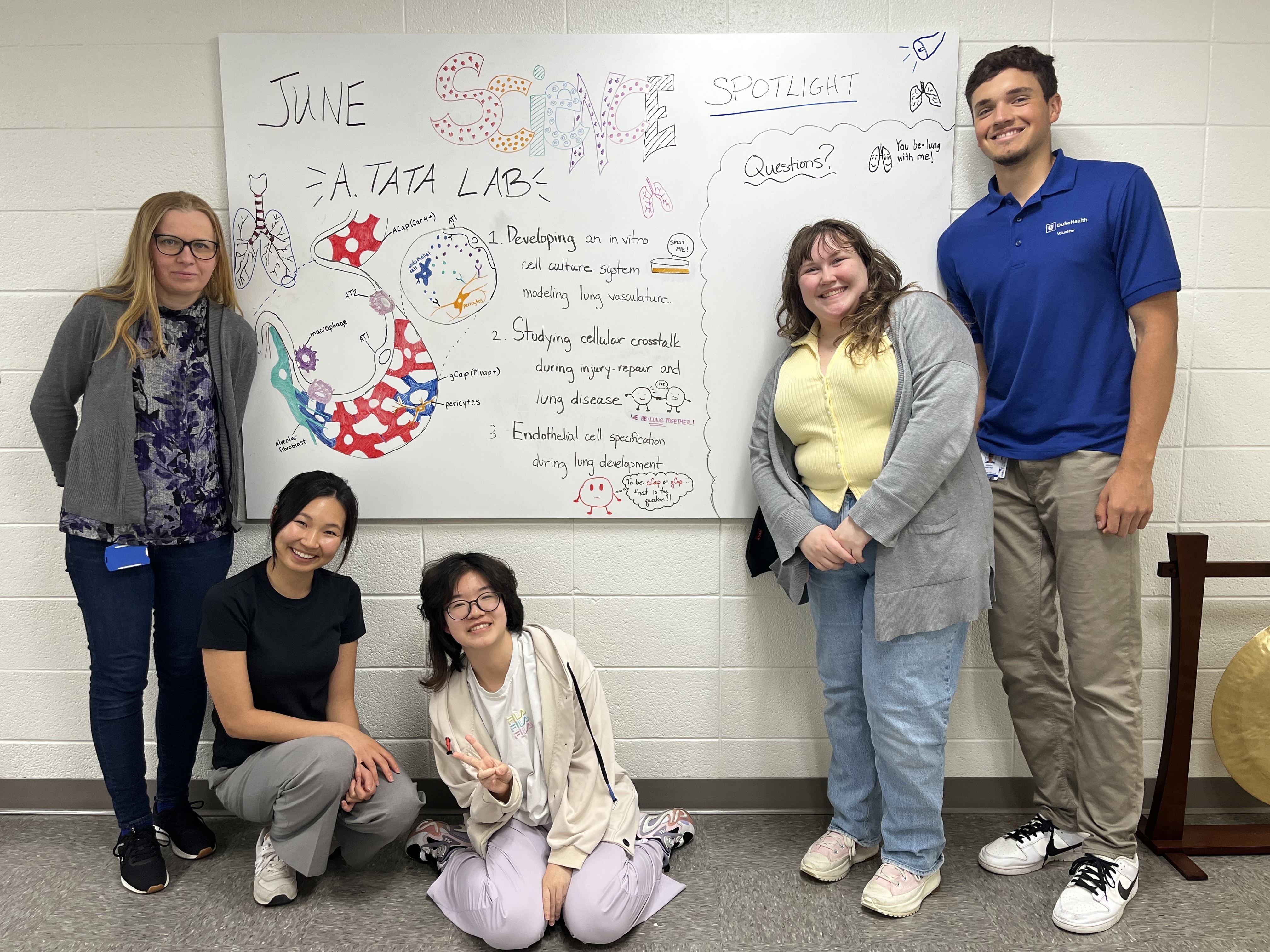 A group of five people stand in front of a white board 