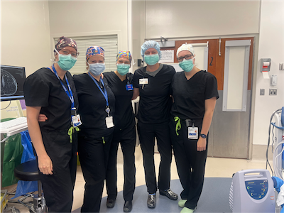 A group of five individuals wearing surgical scrubs and masks pose for a group photo