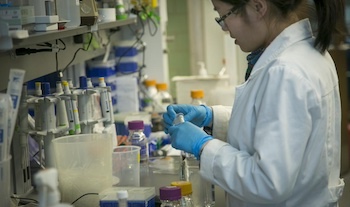A woman in a white lab coat works at a lab station