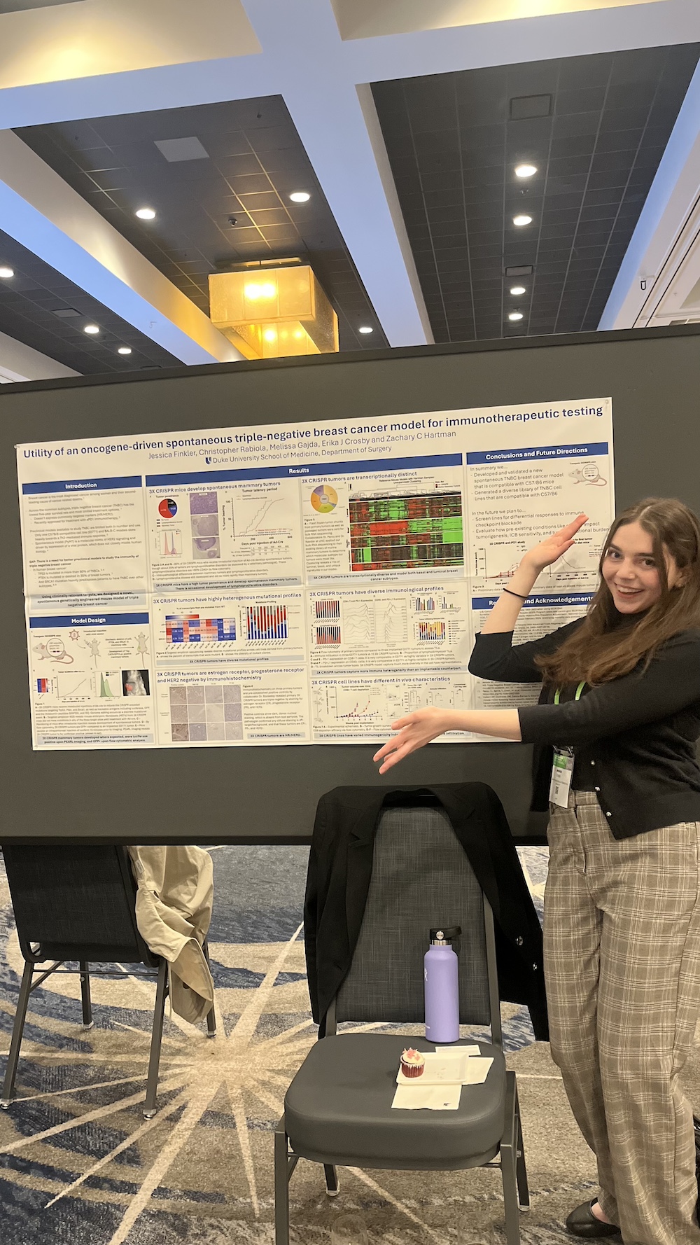A woman stands smiling in front of her scientific research poster