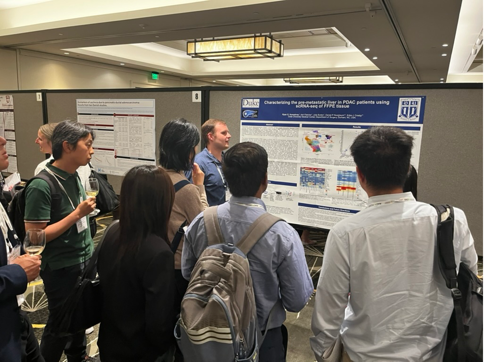 A man presents a scientific research poster to people attending Surgery Research Day