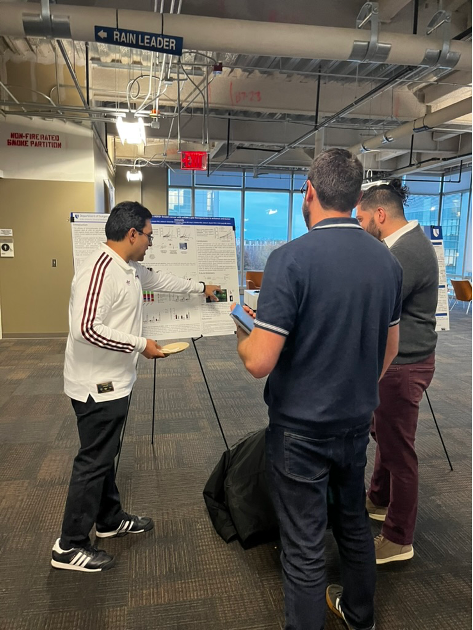 A men presents a scientific research poster to two people