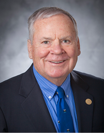 Professional headshot photo of Dr. James R. Urbaniak wearing a black suit jacket over a blue shirt and tie