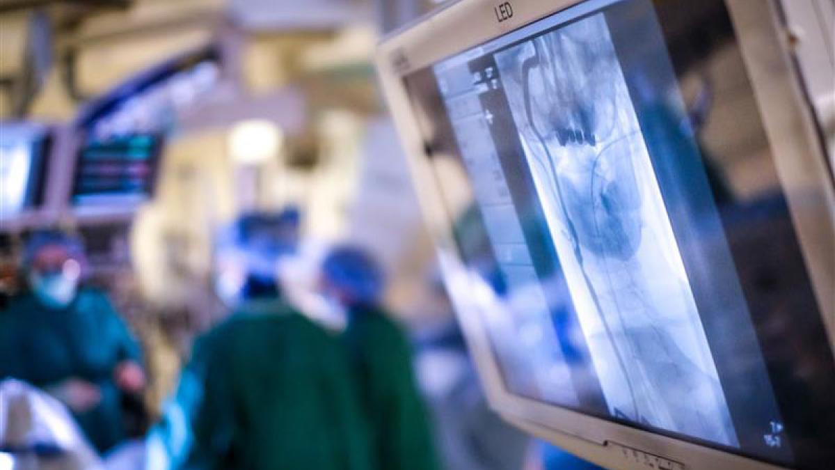 Photo of the OR with an angiogram on a screen in the foreground and the OR team working in the background
