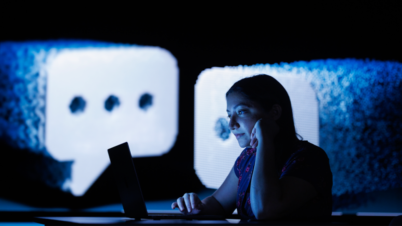 A woman looks at a laptop screen with images of chat bubbles projected behind her