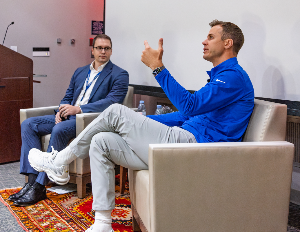 Two men sit in chairs at the front of a lecture hall
