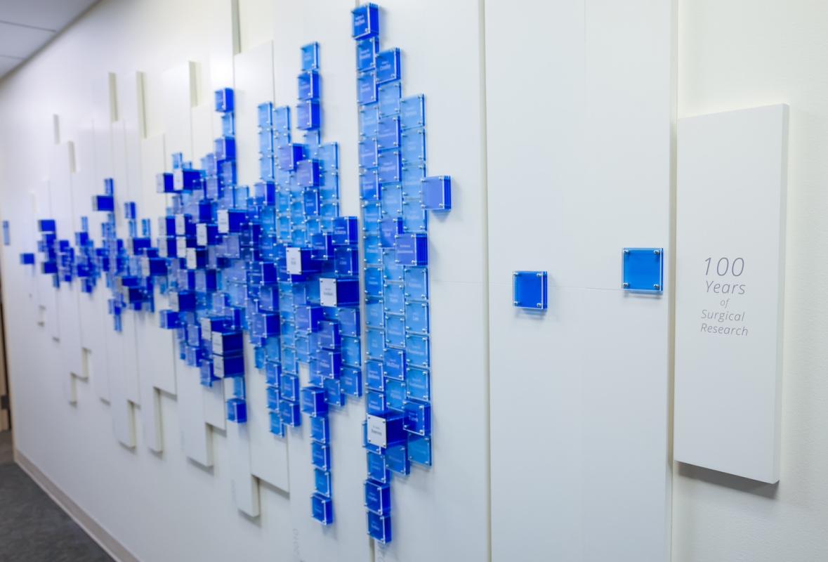 Hundreds of tiles in varying blue shades against a white display background with a title that reads "100 years of surgical research"