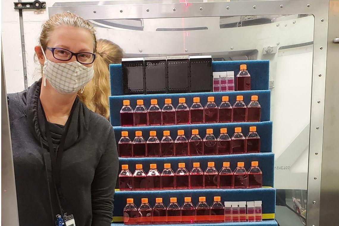 A woman wearing a face mask stands in front of laboratory samples