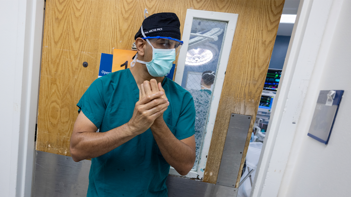 A surgeon wears scrubs, a surgical mask, and a scrub cap as he prepares to enter an operating room