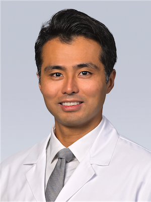 Dr. Daniel Hashimoto poses in his white coat against a grey background for a professional headshot photo.