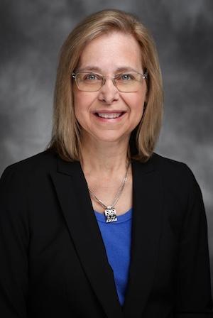 Professional headshot photo of Dr. Debra Sudan, wearing a blue top under a black blazer, against a grey backdrop