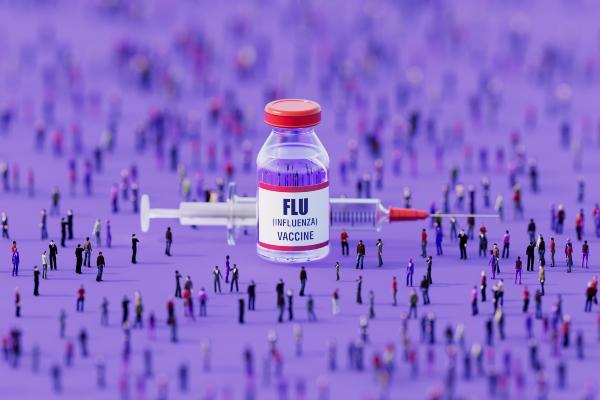 a vial for flu vaccine labeled "FLU" sits on a table in front of a syringe 