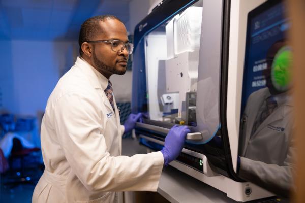 Dr. Wilton Williams in a white lab coat and sterile gloves in his research laboratory