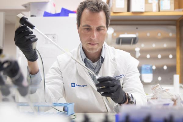 A man in a white lab coat and black gloves works in a laboratory