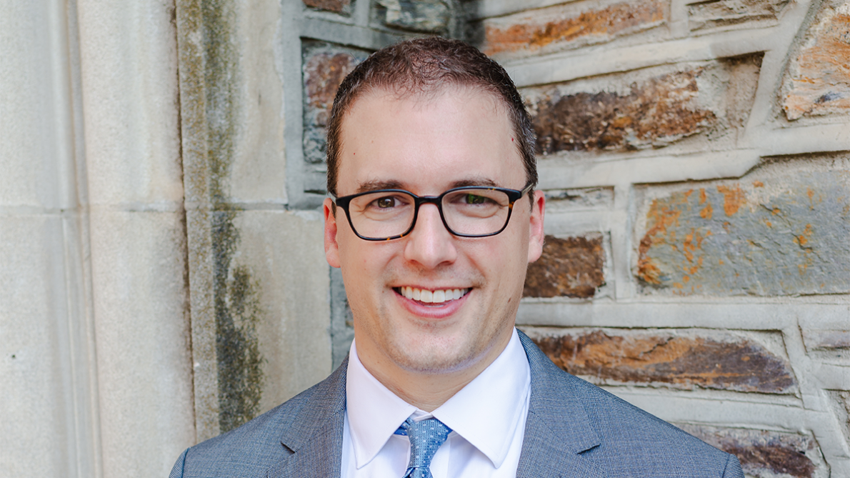 Dr. Ryan Antiel smiles in front of an exterior brick wall