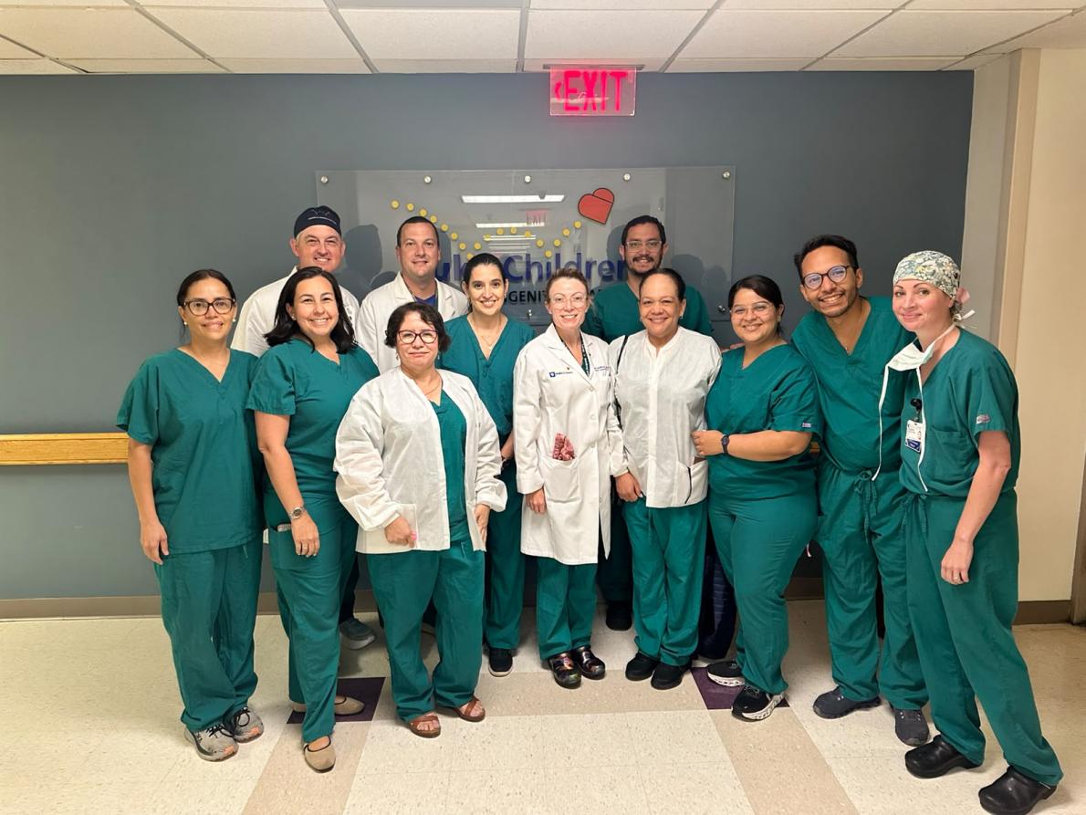 A group of 12 surgeons, all wearing teal scrubs and some in white coats, pose together for a group photo inside the Duke Children's Hospital.