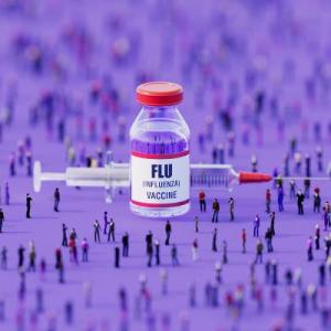 a vial for flu vaccine labeled "FLU" sits on a table in front of a syringe 