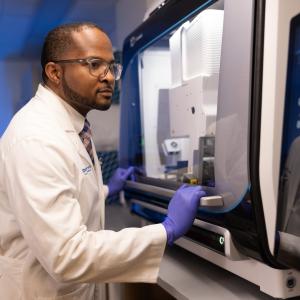 Dr. Wilton Williams in a white lab coat and sterile gloves in his research laboratory
